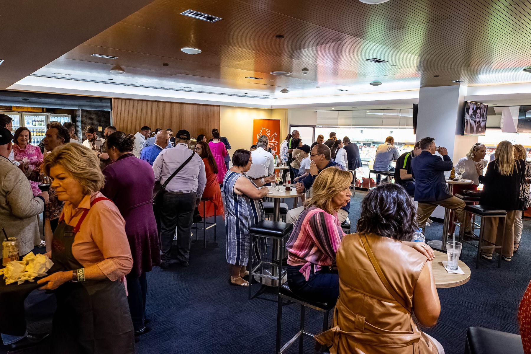 Guests mingling in a Brisbane Roar hospitality lounge with the pitch in view